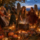 Celebración de Samhain con mujeres adultas bailando alrededor de un caldero, calabazas, velas y calaveras decorativas en un bosque al atardecer